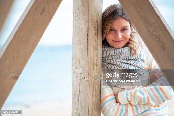 smiling young woman leaning on wood at beach - cachecol imagens e fotografias de stock