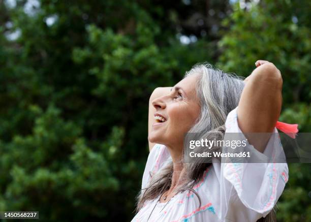 happy mature woman with hands behind head at forest - grijs haar stockfoto's en -beelden