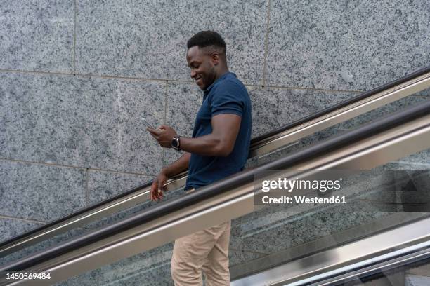 smiling man using smart phone moving down on escalator - escalator side view stock pictures, royalty-free photos & images