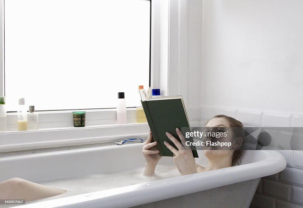 Woman relaxing at home reading a book in the bath