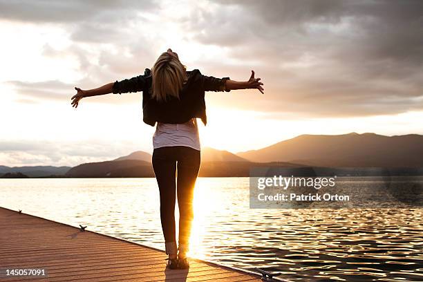 a beautiful young woman looking into the distance holds her arms out embracing the sunset over a lake in idaho. - pend orielle lake stock pictures, royalty-free photos & images