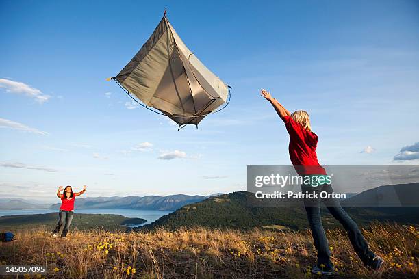 two women throwing a tent at sunset on a camping trip above a lake in idaho. - pend orielle lake stock pictures, royalty-free photos & images