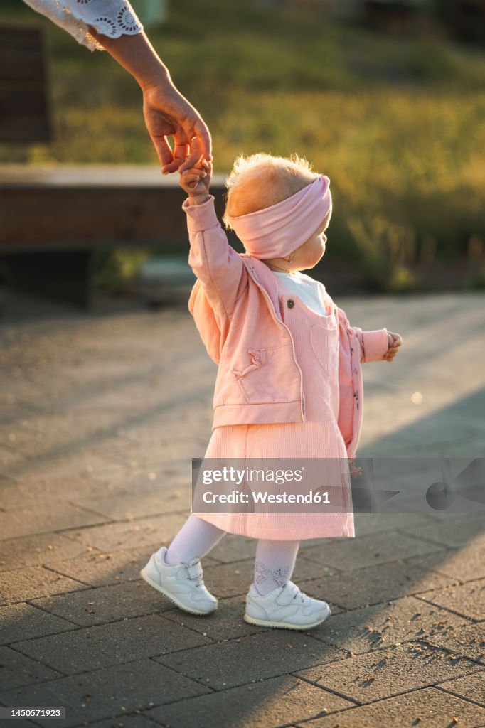 Girl holding hand of mother on footpath