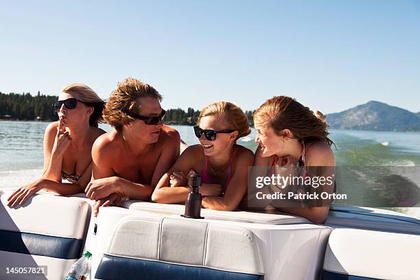 four young adults laughing and smiling on the back of a wakeboard boat on a lake in idaho. - pend orielle lake stock pictures, royalty-free photos & images