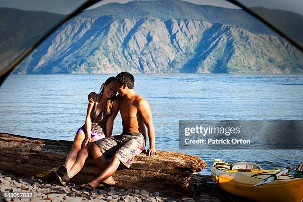 a happy young adult couple smile and laugh on a camping trip next to a lake in idaho. - pend orielle lake stock pictures, royalty-free photos & images