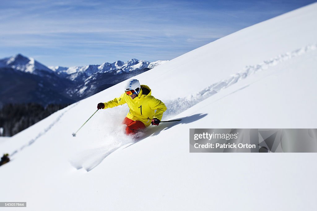 A athletic skier rips fresh powder turns on a sunny day in Colorado.