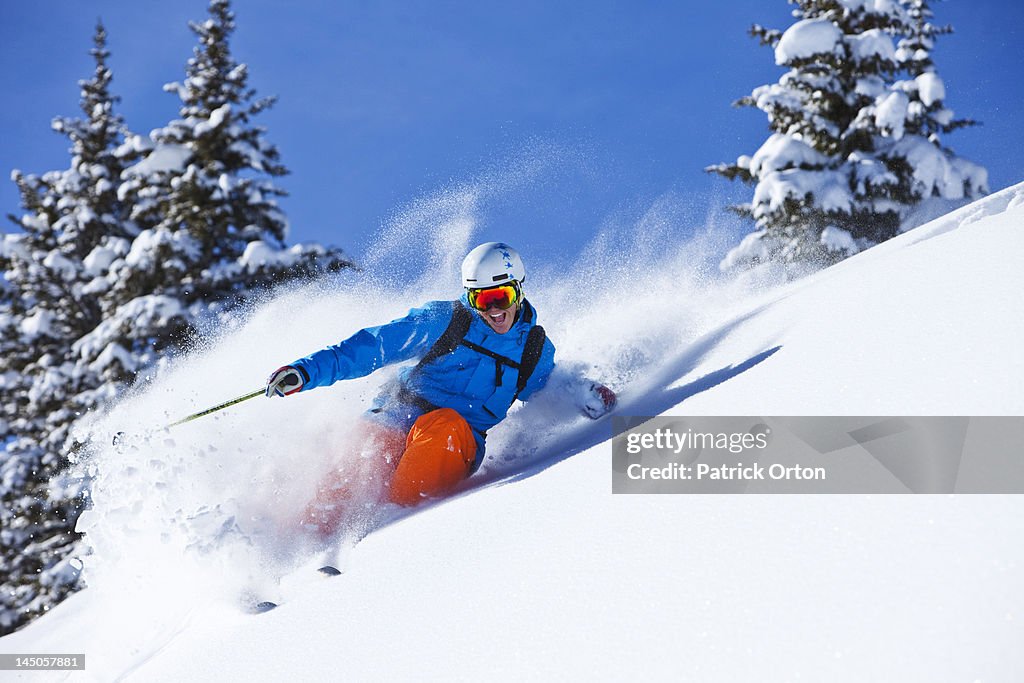 A athletic skier smiling rips fresh powder turns in the backcountry on a sunny day in Colorado.