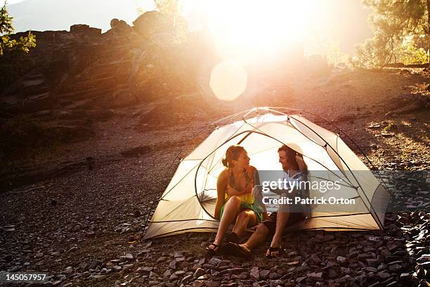 a young adult couple laugh and smile while sitting in a tent on a camping trip in idaho. - pend orielle lake stock pictures, royalty-free photos & images
