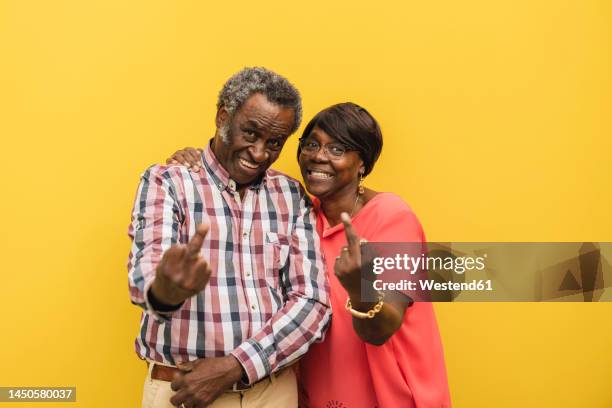 smiling senior couple showing obscene gesture against yellow background - old lady middle finger - fotografias e filmes do acervo