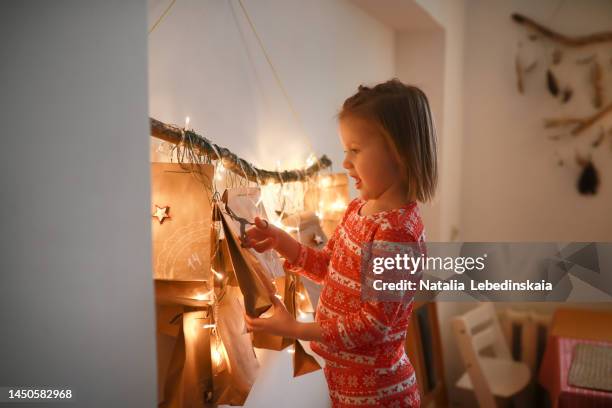 4 year old child in christmas pajamas cuts off opens package with advent calendar. - child with advent calendar 個照片及圖片檔