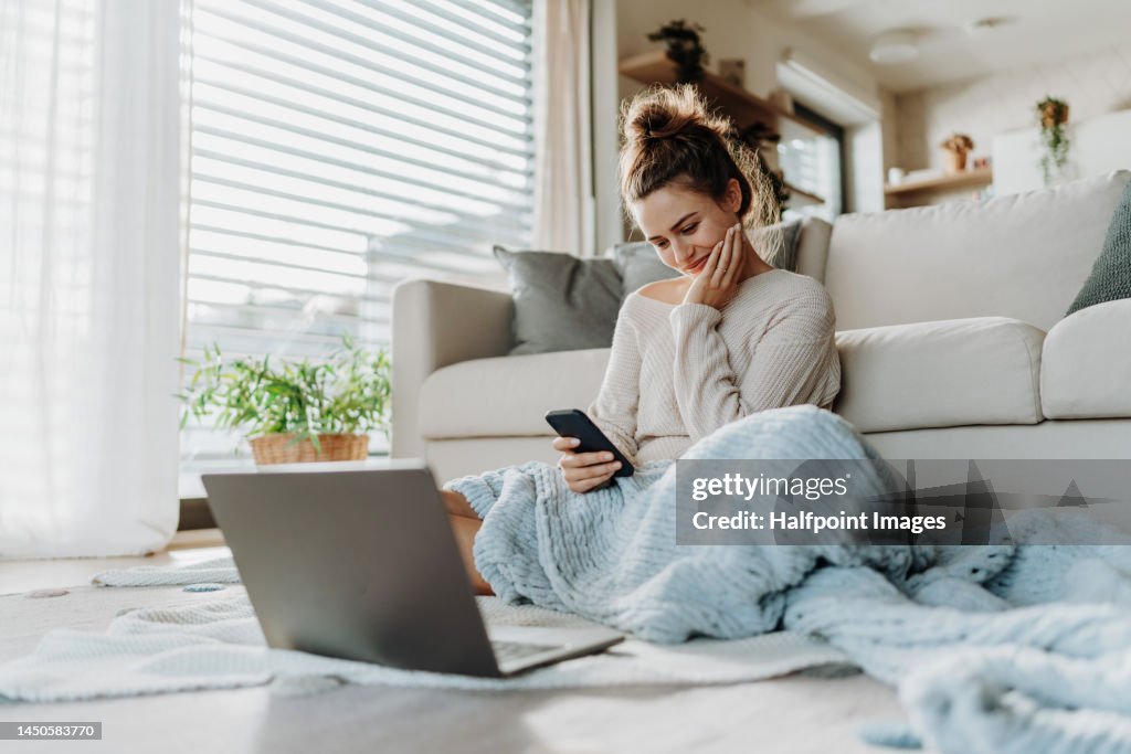 Young woman resting in living room with smartphone and laptop.