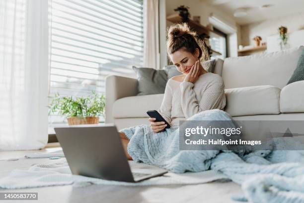 young woman resting in living room with smartphone and laptop. - gemütlich stock-fotos und bilder