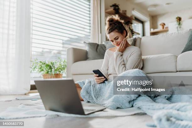 young woman resting in living room with smartphone and laptop. - winter woman phone stock-fotos und bilder