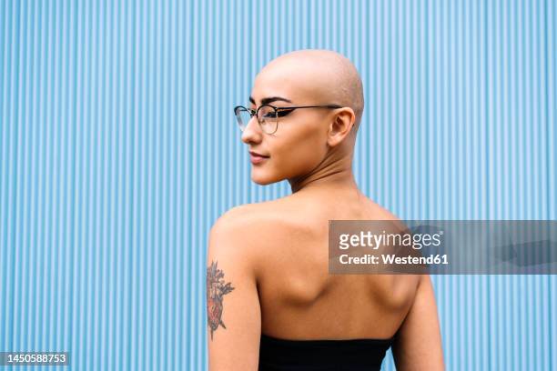 woman with shaved head in front of blue wall - tattoo shoulder stock pictures, royalty-free photos & images