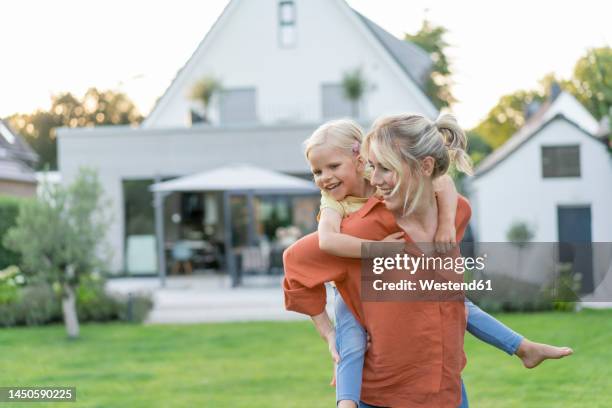 happy mother giving piggyback ride to daughter in garden - happy family home outdoors stockfoto's en -beelden