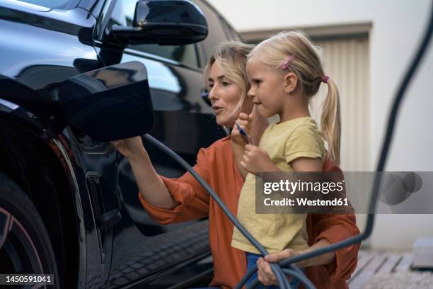 girl holding credit card by mother charging electric vehicle in front yard - electric car home stock pictures, royalty-free photos & images