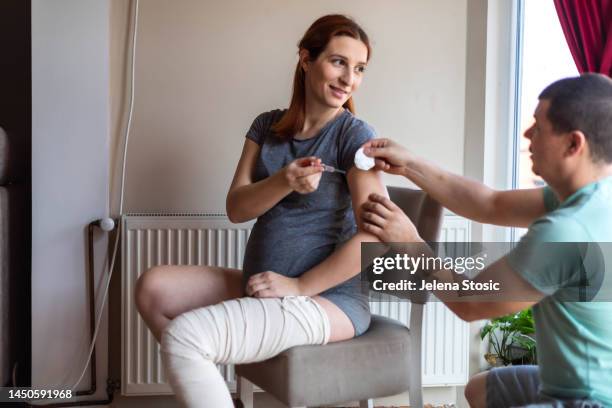 a pregnant woman gives her husband a syringe. the man cleans the area with alcohol before injecting the woman's arm. - preventive care stock pictures, royalty-free photos & images