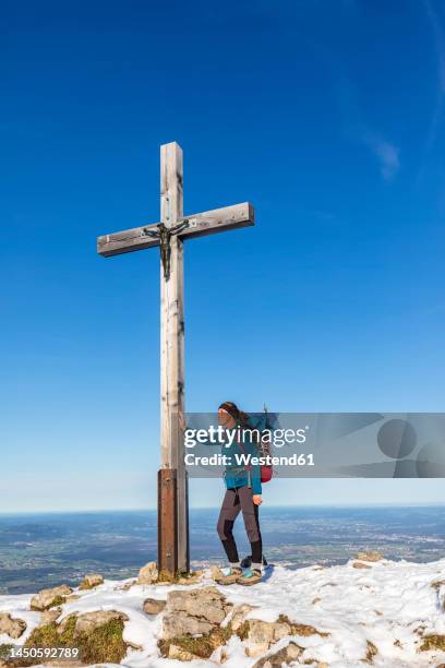 germany, bavaria, female hiker standing in front of summit cross on hochries mountain - gipfelkreuz stock-fotos und bilder