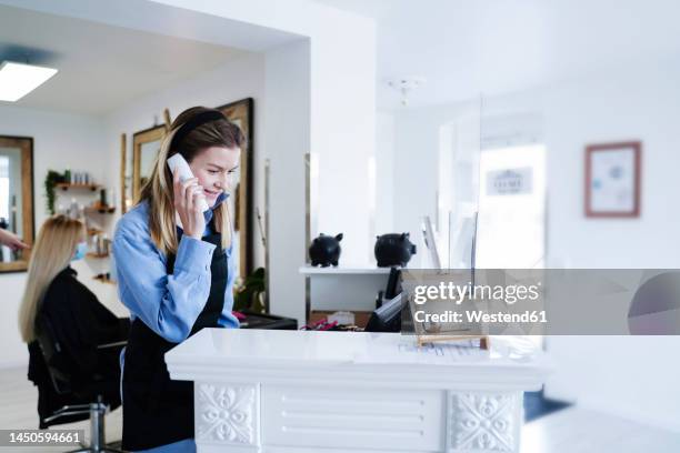 smiling hairdresser talking on phone at reception desk in salon - salon reception stock-fotos und bilder