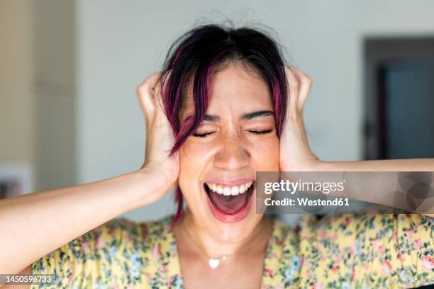 young woman with head in hands screaming at home - handen over de oren stockfoto's en -beelden