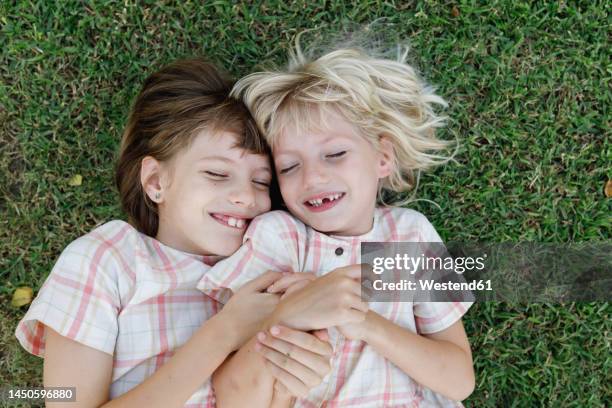 smiling girl with sister lying on grass - zustand stockfoto's en -beelden