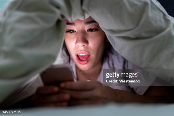 surprised young woman using smart phone on bed at home - shock stock photos et images de collection