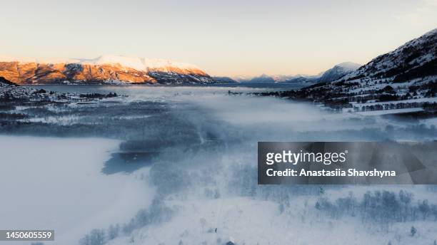 aerial view of a woman walking at snowcapped road by the shelter in forest with frozen lake and idyllic mountain view during sunrise in norway - pure stockfoto's en -beelden