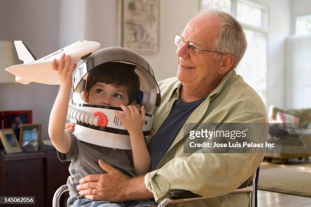 caucasian boy in space helmet sitting on grandfather's lap - astronaut helm stock pictures, royalty-free photos & images