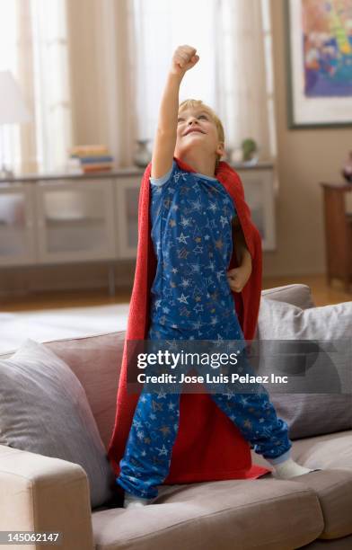 caucasian boy in superhero costume standing on sofa - blonde cheering stock-fotos und bilder