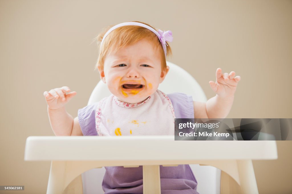 Caucasian baby girl crying in high chair