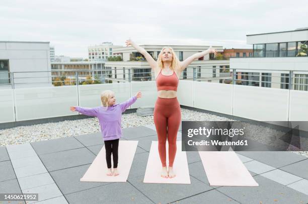 daughter with arms outstretched looking at mother practicing yoga on rooftop - mom daughter white stock-fotos und bilder