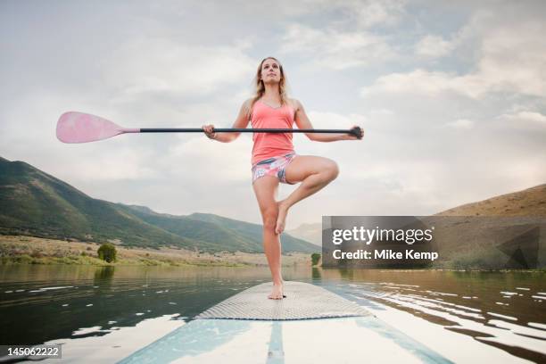 caucasian woman on stand up paddle board - practioners enjoy serenity of paddleboard yoga stockfoto's en -beelden