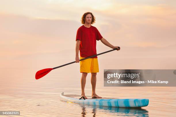 caucasian man standing on paddle board - paddle board men imagens e fotografias de stock