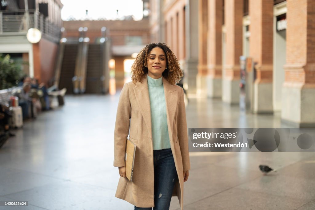 Smiling businesswoman holding laptop commuting at station