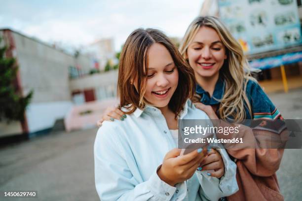 smiling mother with daughter using mobile phone - celular escola imagens e fotografias de stock