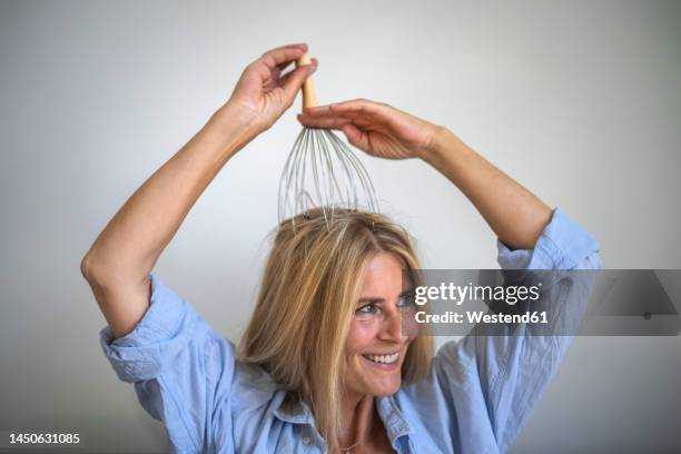 smiling mature woman head massaging with orgasmatron in front of wall - head massage fotografías e imágenes de stock