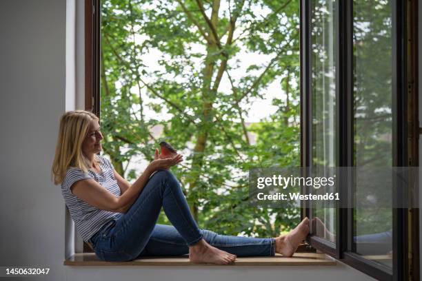 mature woman holding bird sitting on window at home - one animal stock pictures, royalty-free photos & images