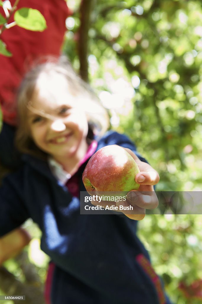 Smiling girl offering fruit in tree