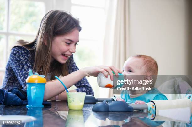 girl feeding baby brother at table - baby sibling stock pictures, royalty-free photos & images