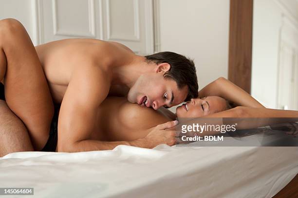 man kissing nude girlfriend in bed - frau brust erotisch stock-fotos und bilder