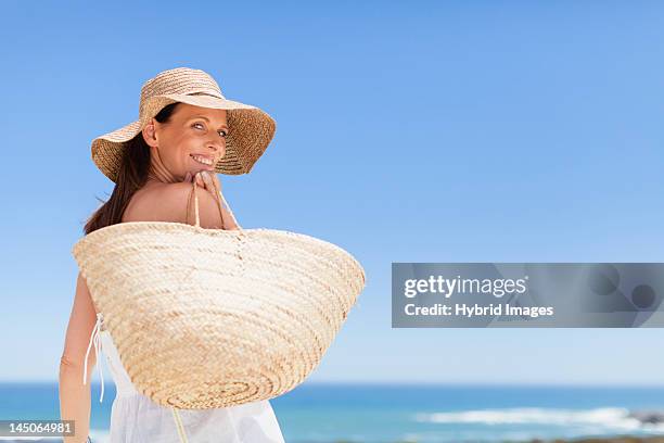 woman carrying straw bag outdoors - cappello per il sole foto e immagini stock