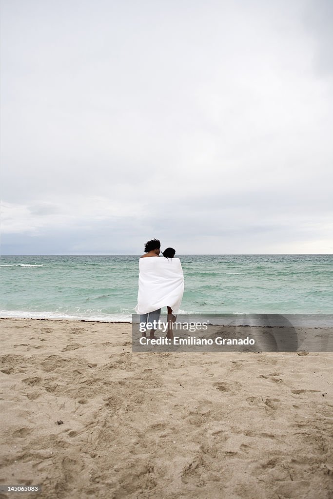 A young couple wrapped in a beach towel standing on the beach