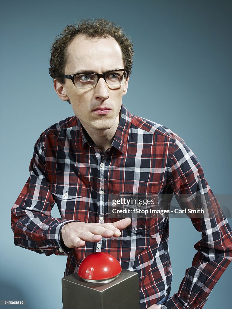 A nerdy guy with his hand poised above a red game show buzzer