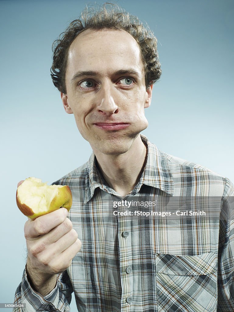 A man with a cheek bulging with a bite of apple, looking to the side