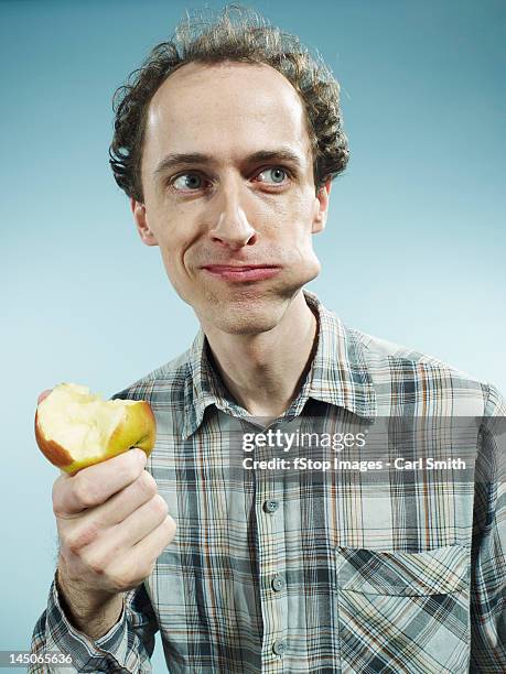 a man with a cheek bulging with a bite of apple, looking to the side - mejilla fotografías e imágenes de stock