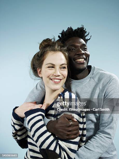 a smiling young man embracing his smiling girlfriend from behind - couples studio portrait stock-fotos und bilder