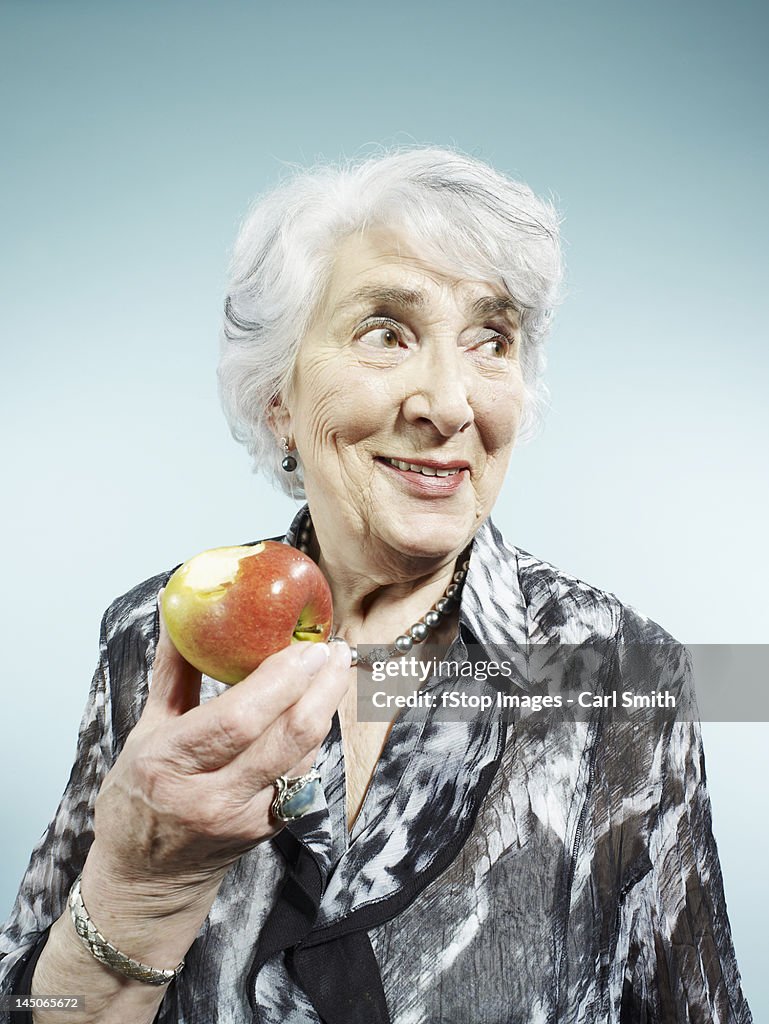 A senior woman holding an apple with a bite out of it