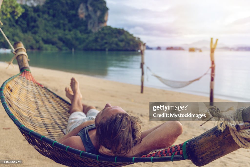 Man relaxing on hammock by the beach at sunrise