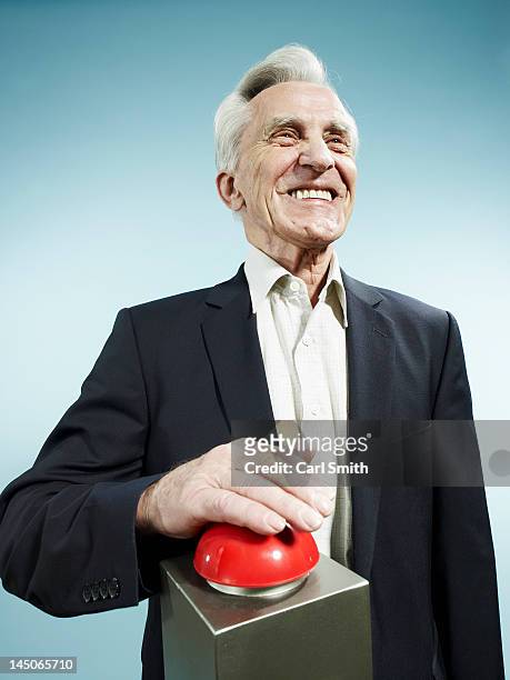 a grinning senior man pushing a red game show buzzer - buzzer stock-fotos und bilder