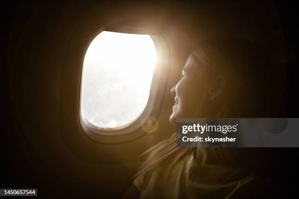 glückliche frau, die genießt, während sie durch das flugzeugfenster schaut. - economy class stock-fotos und bilder